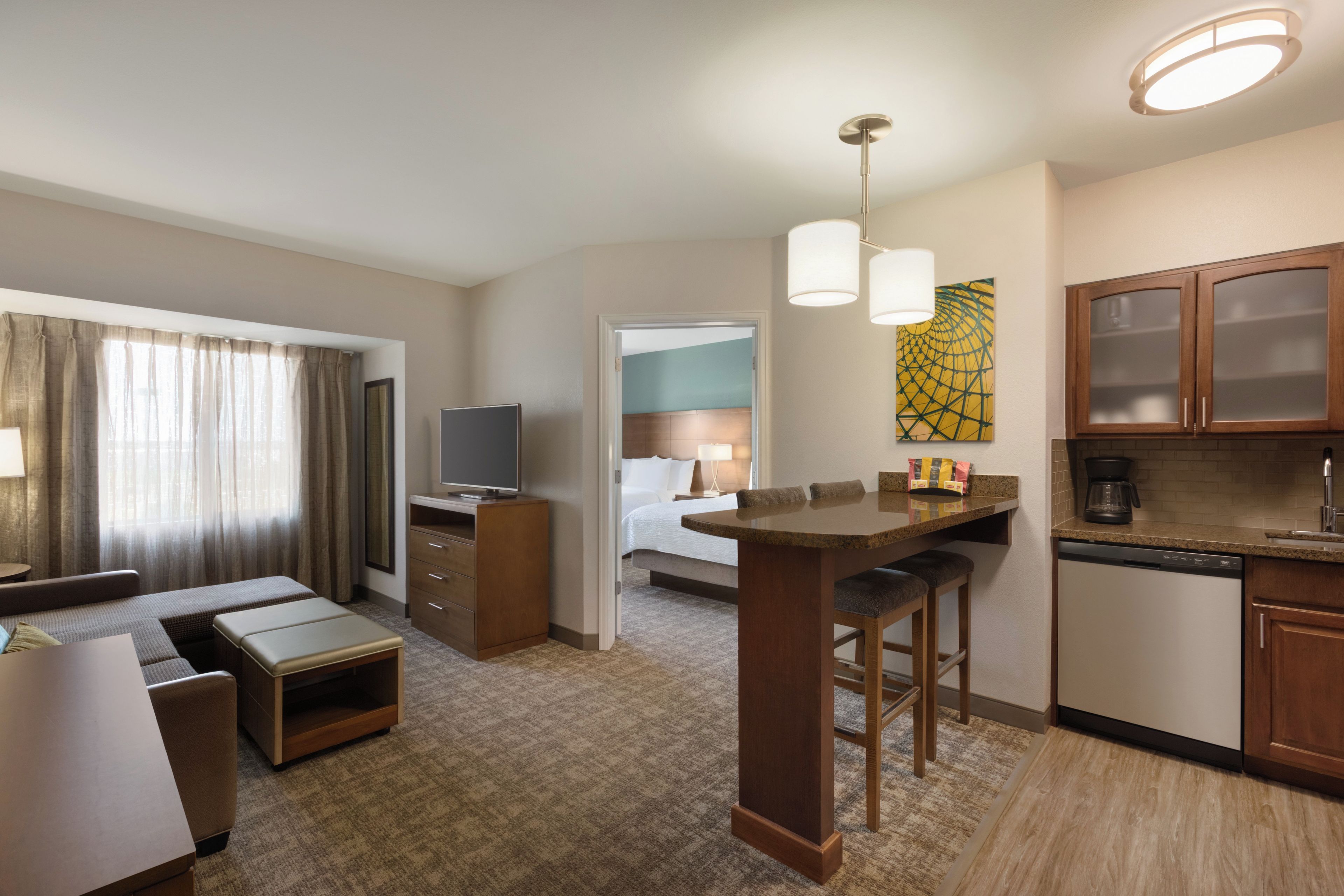 A hotel room with a kitchenette, a dining area, a TV, a bed, and a bathroom visible through an open door.