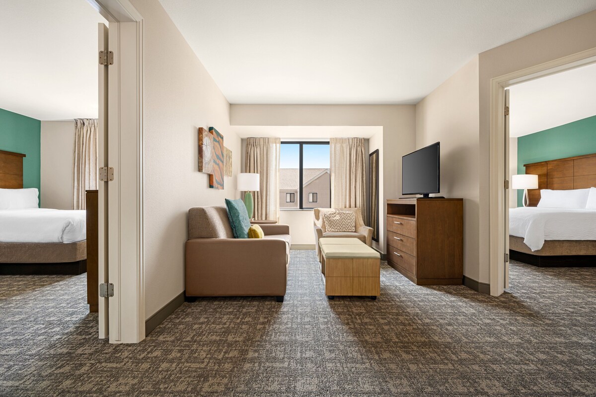 A hotel room with two beds, a sofa, a TV, and a desk.