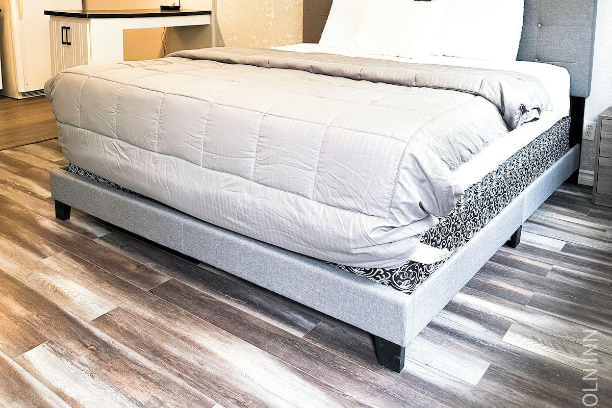 Un dormitorio moderno con una cama grande, un escritorio empotrado y una kitchenette al fondo.