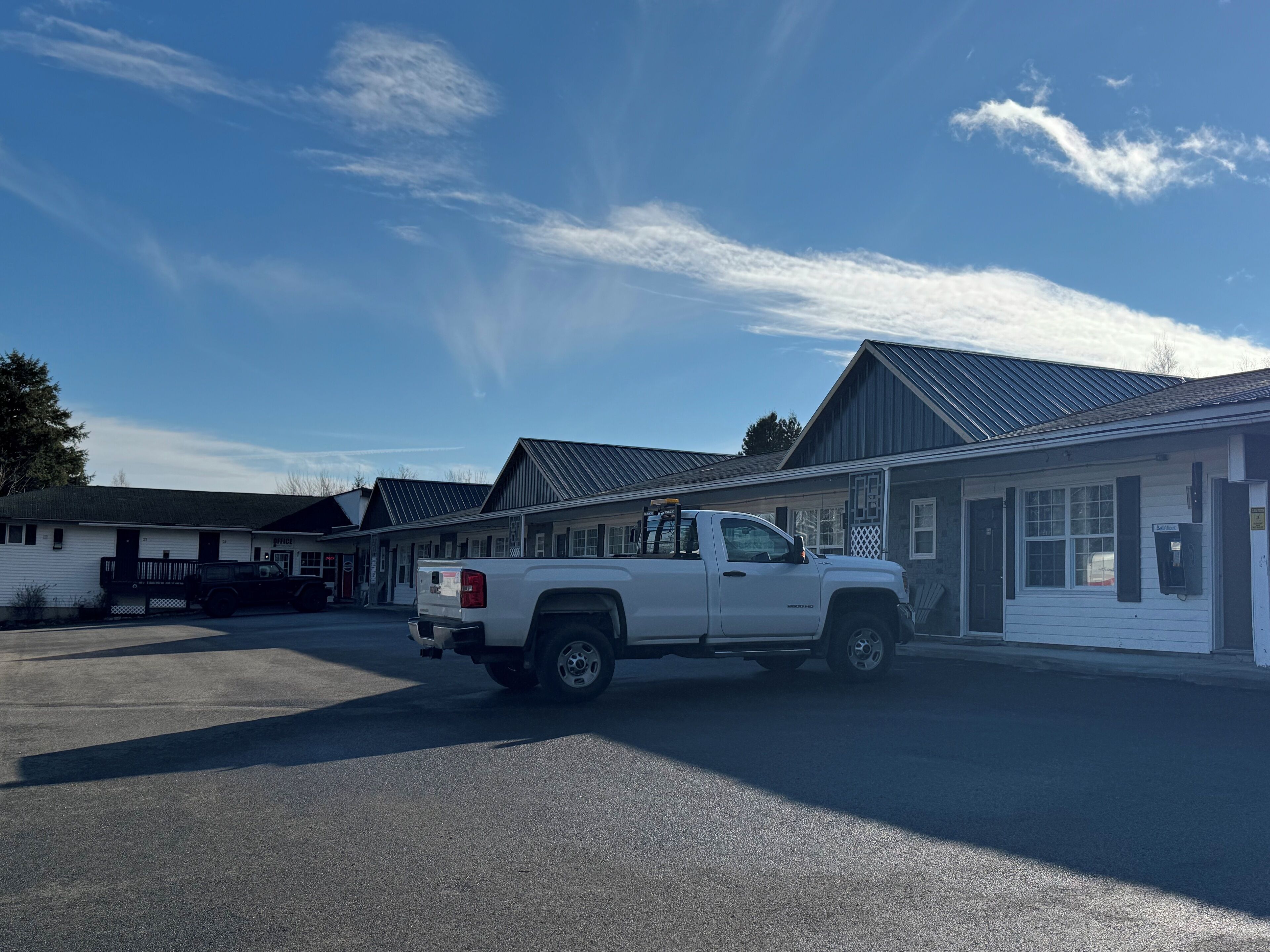 A white pickup truck parked in front of a row of buildings with a metal roof.