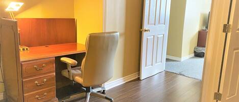 A room with a wooden desk, a chair, a filing cabinet, and a door.
