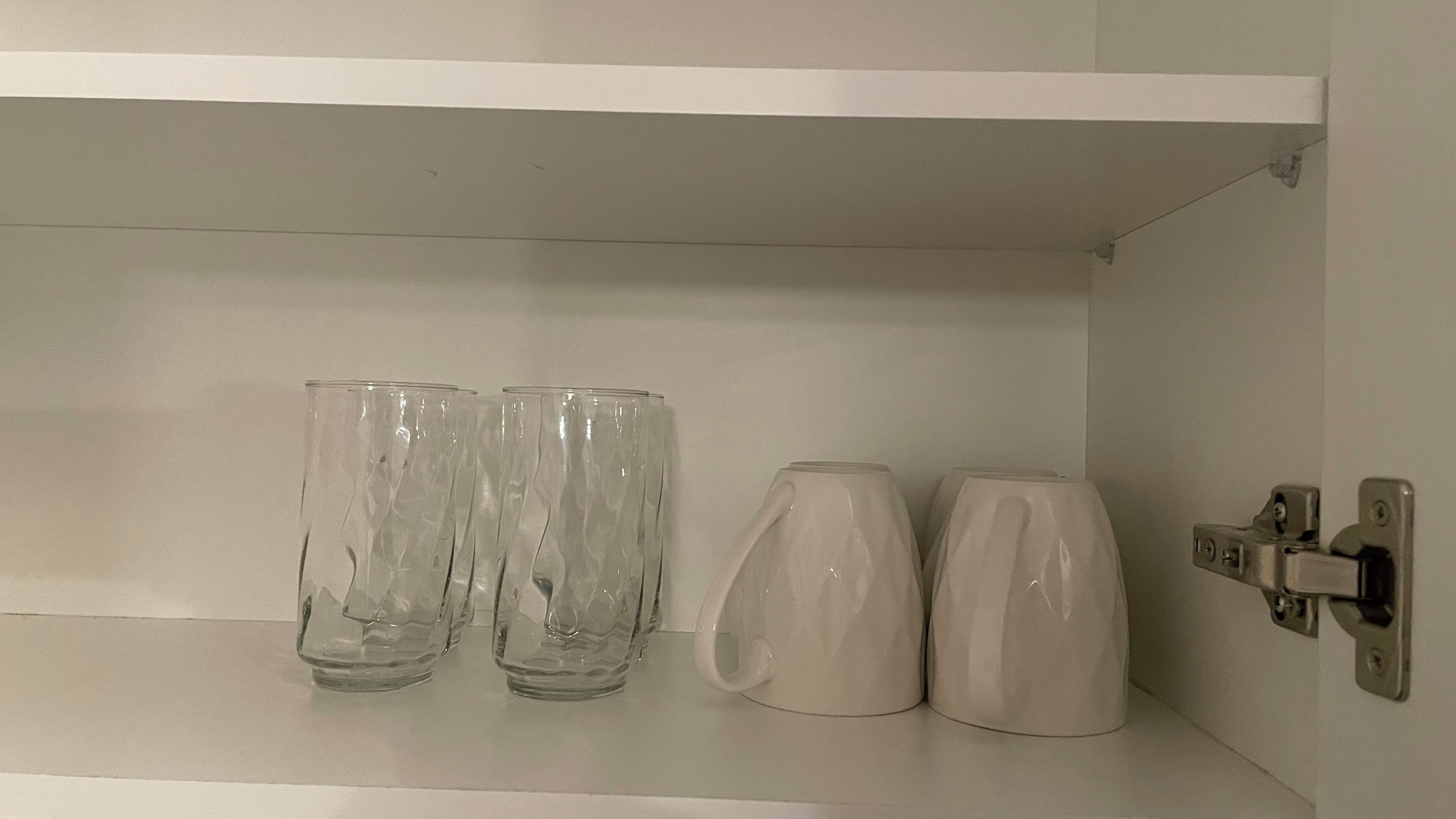 A white shelf with three clear glasses and two white mugs.