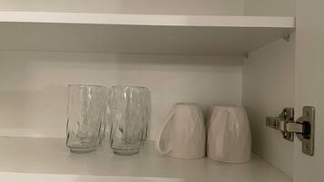 A white shelf with three clear glasses and two white mugs.