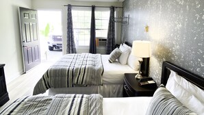 A hotel room with two beds, a nightstand with a lamp, a wall-mounted TV, and a window with curtains.