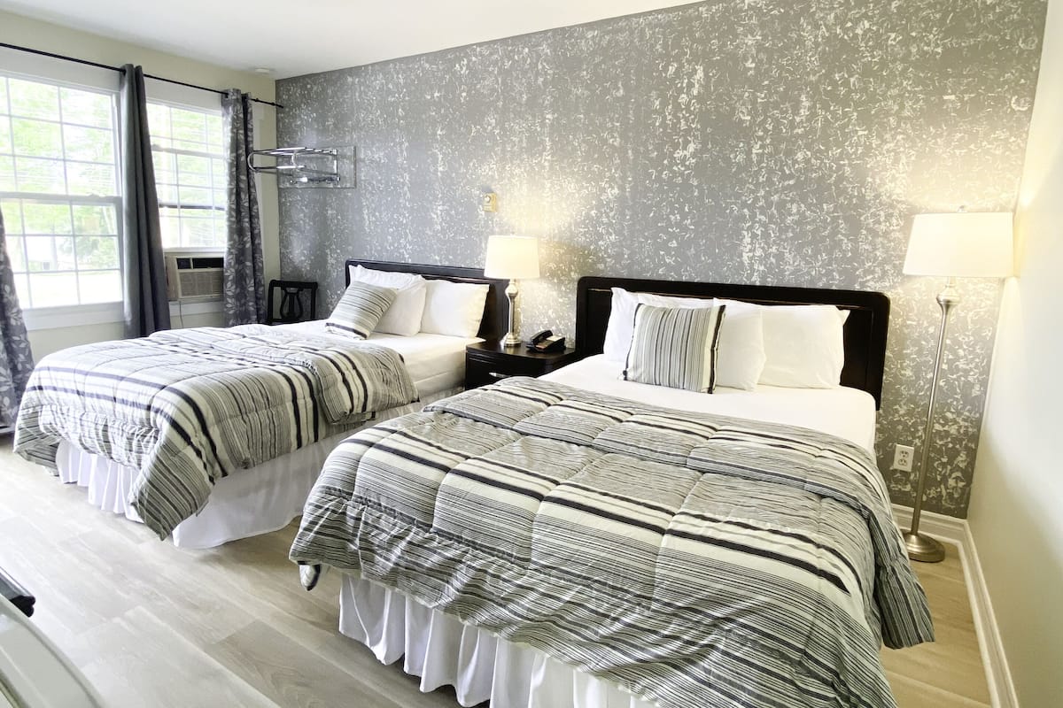 Habitación doble con dos camas, un ventanal grande y una pared con textura.