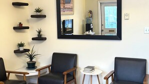 A room with two black leather chairs, a small white table, a mirror, and a clock on the wall.