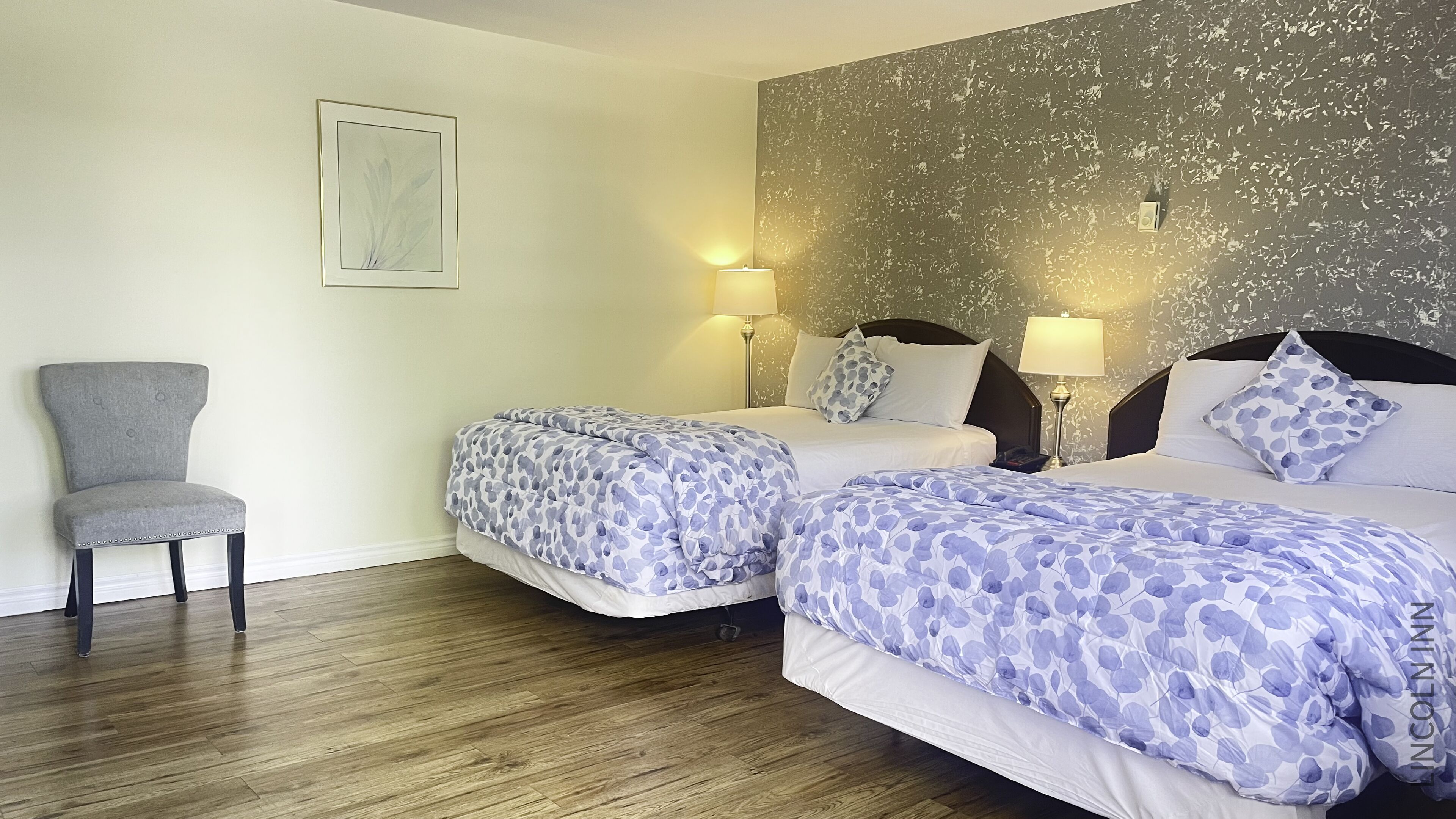 A hotel room with two beds, a chair, and a wall with a textured pattern.