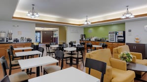Un espace repas moderne avec plusieurs tables et chaises, un coin café et une cuisine en arrière-plan.