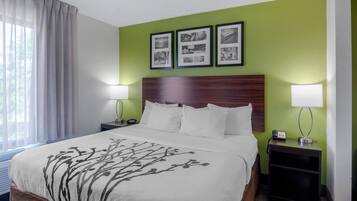 A hotel room with a bed, two bedside tables, a nightstand, a lamp, and a window with curtains.