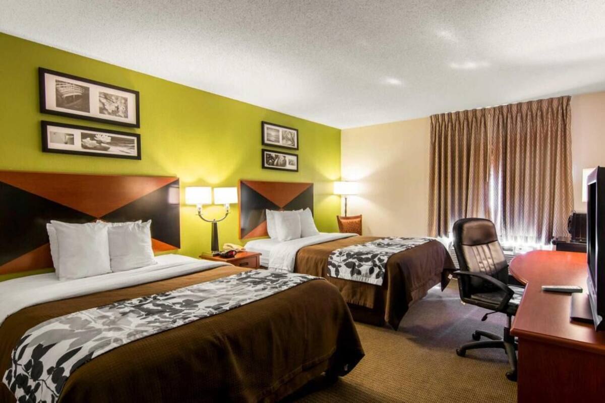 A hotel room with two beds, a desk with a chair, a television, and framed pictures on the wall.