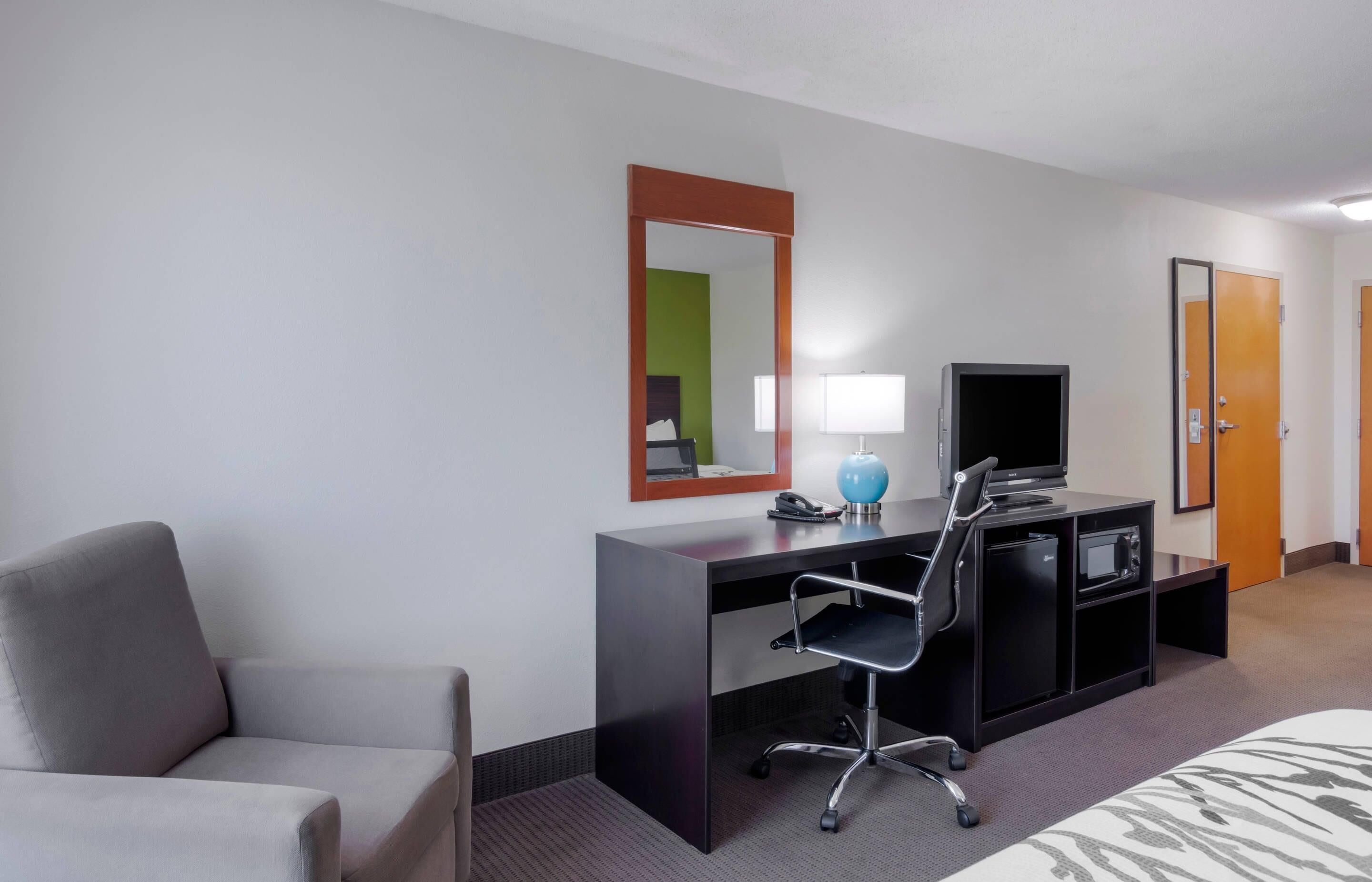 A hotel room with a desk, chair, television, and a bed.