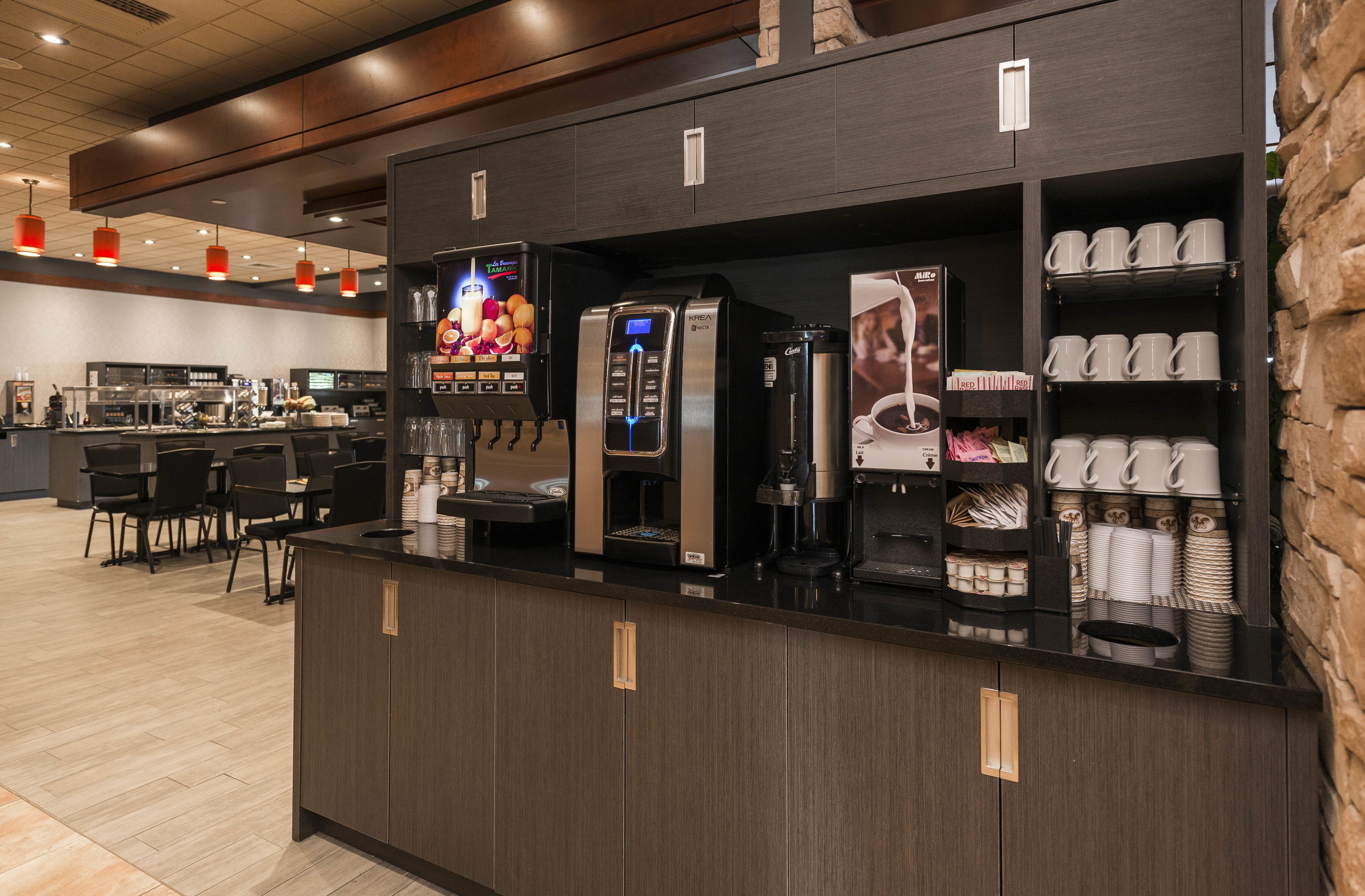 Una estación de café con varias máquinas de café, una exhibición de tazas y una zona de estar con mesas y sillas.