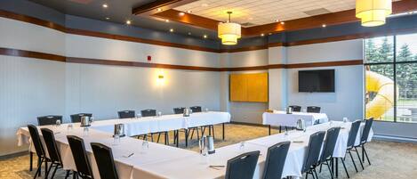 A conference room with long tables, chairs, and a projector screen.