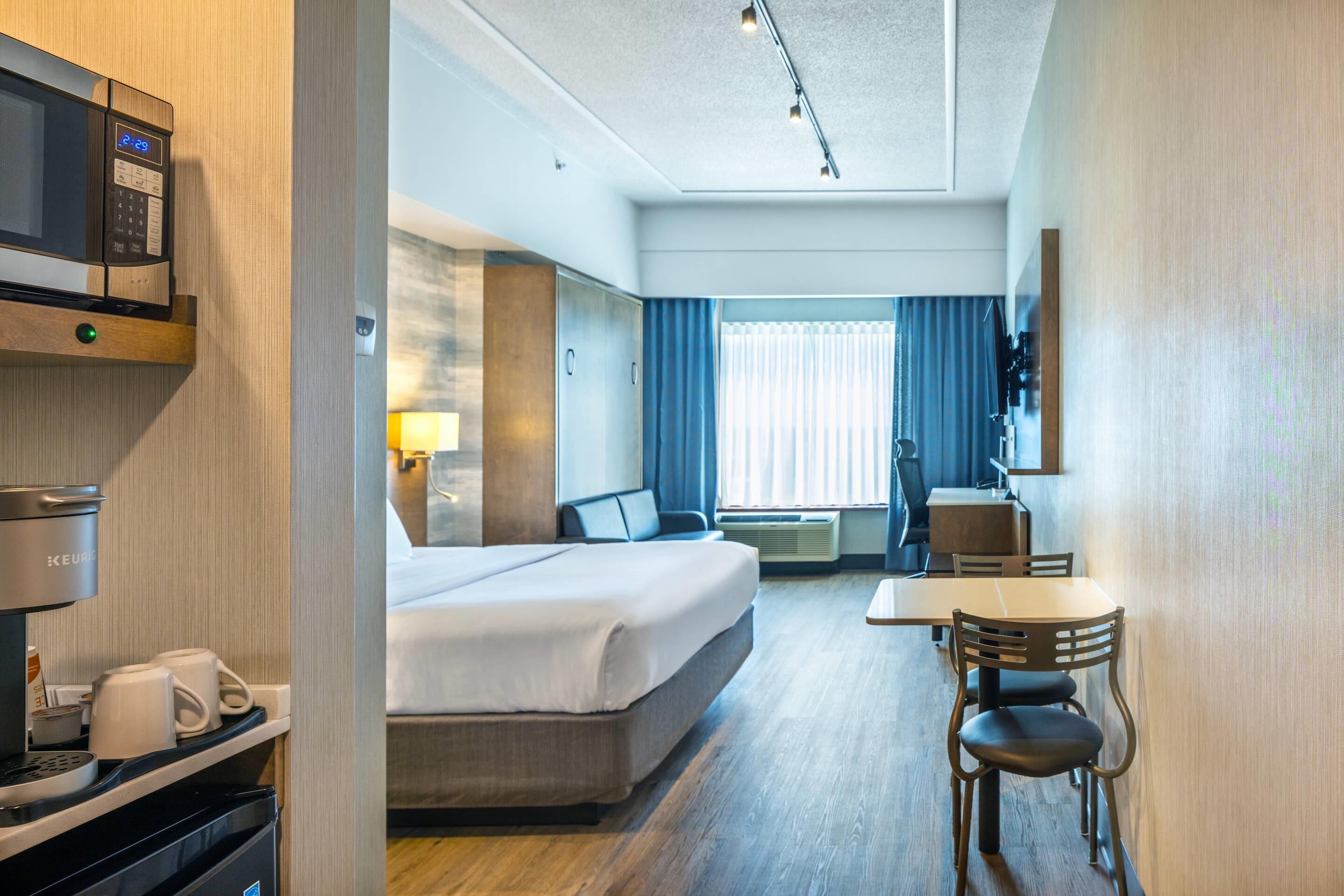 A hotel room with a bed, a desk, a chair, a microwave, and a coffee machine.