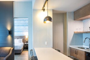 A modern hotel room with a bed, bedside table, lamp, and a view of the sky.