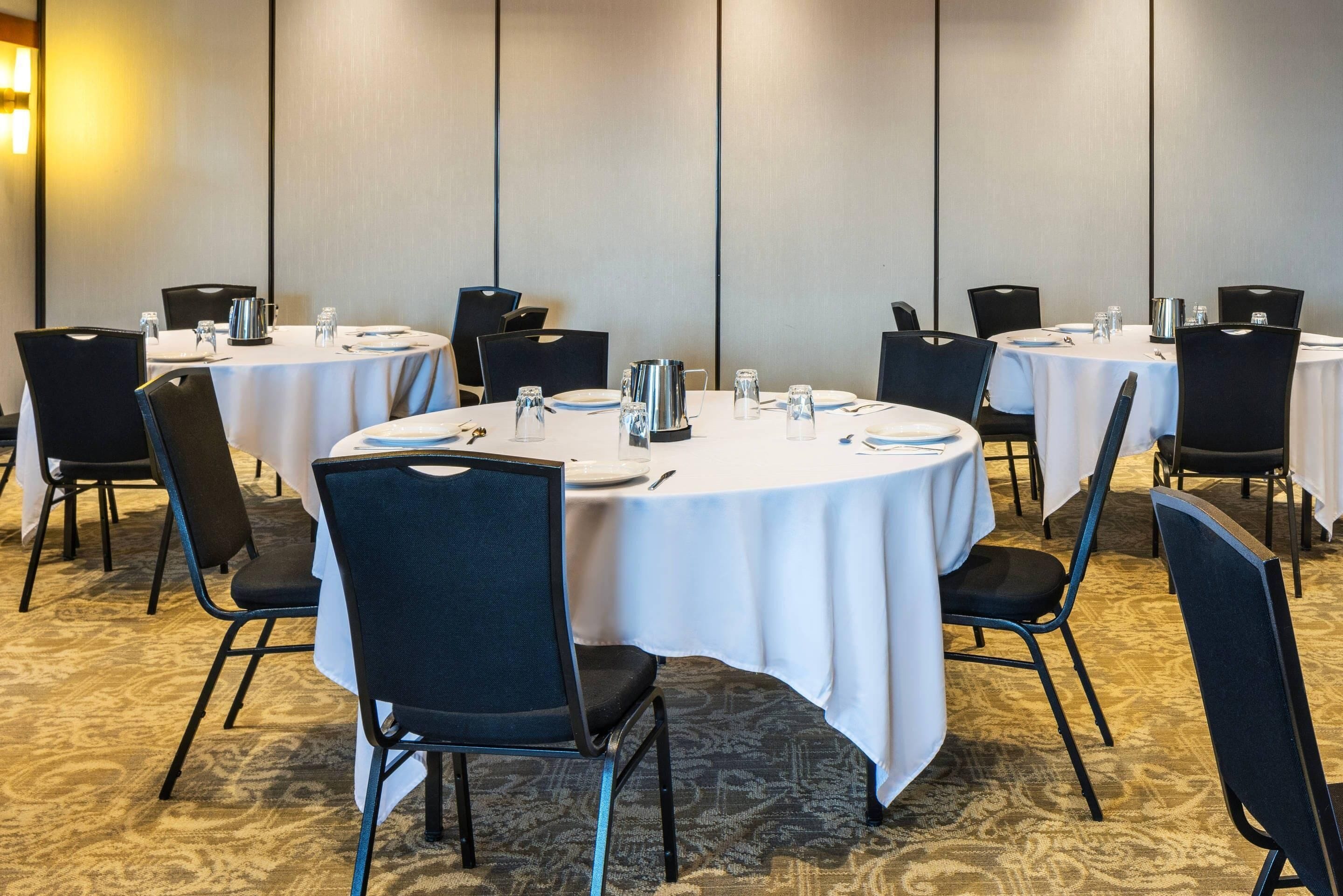 A conference room with round tables, black chairs, and white tablecloths.