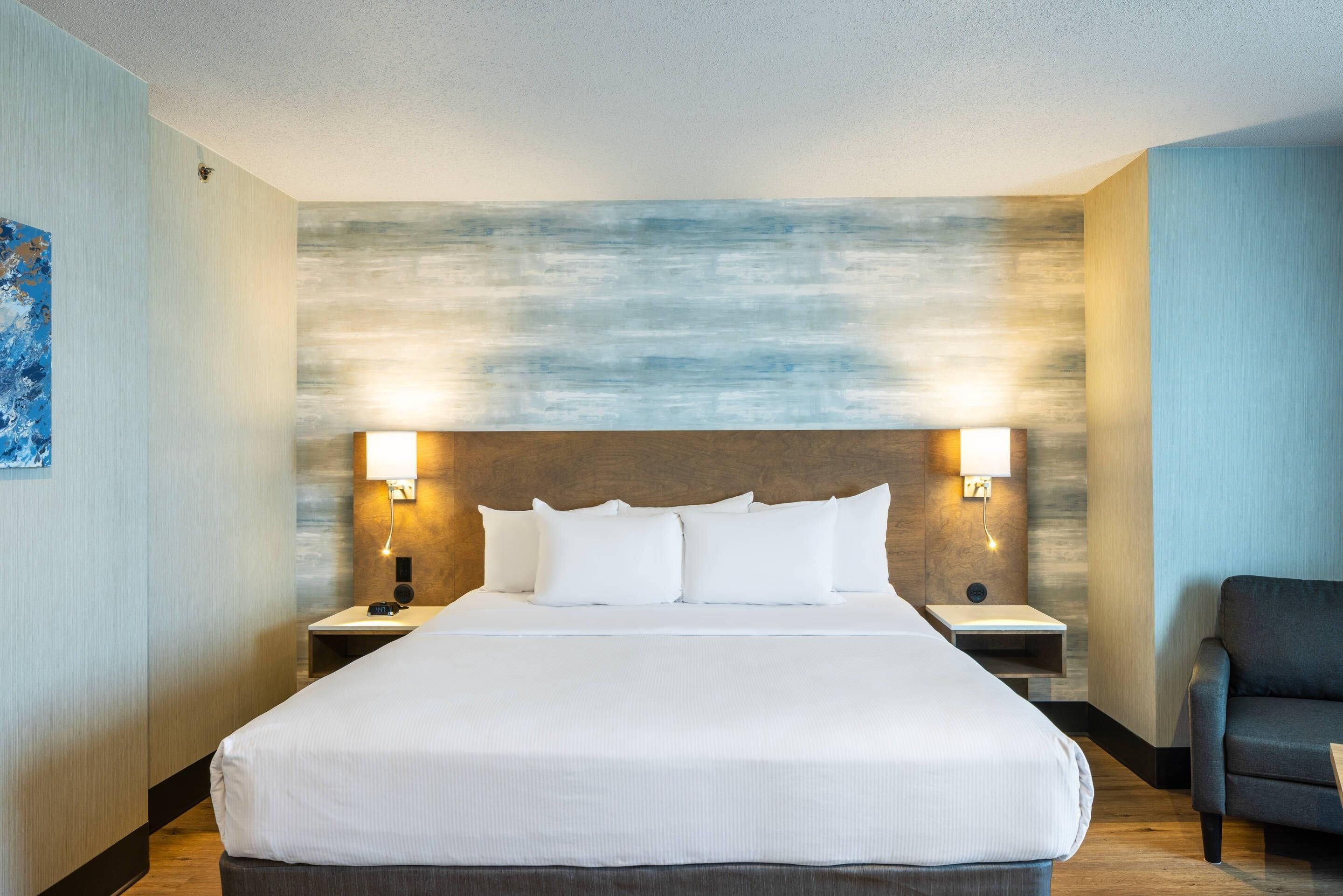 A hotel room with a large bed, two bedside tables, a chair, and a wall with a textured design.