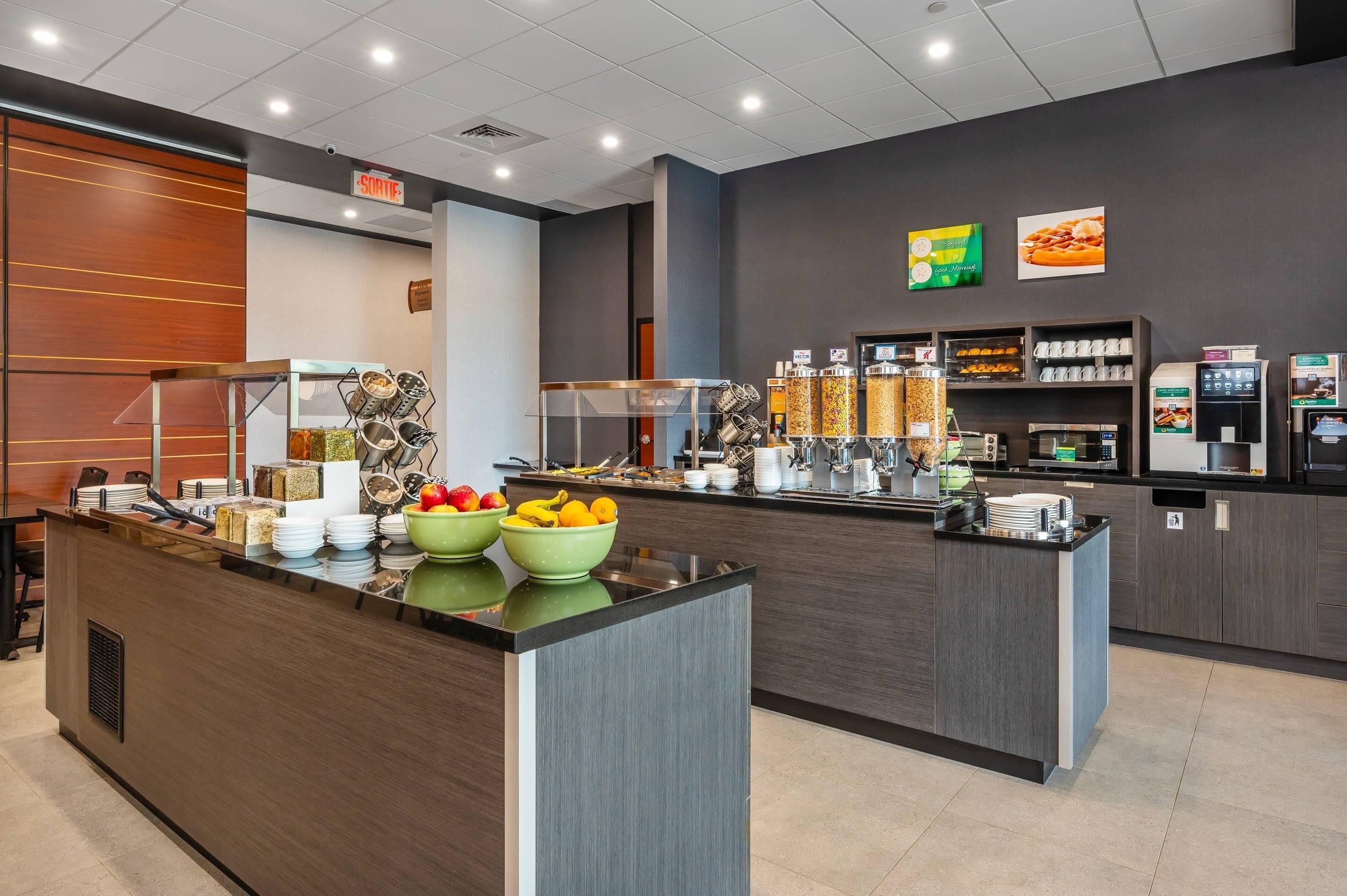 A modern breakfast bar with a variety of food items and beverages, including bowls of fruit and a coffee machine.
