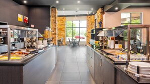 A modern buffet area with multiple food stations, a seating area with tables and chairs, and a view of the outdoors through large windows. - Quality Inn & Suites Levis (Levis)