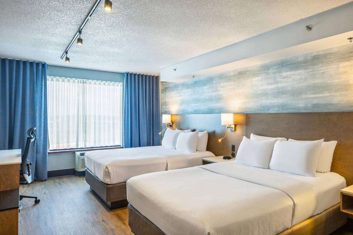 A hotel room with two beds, a desk, and a window with curtains.