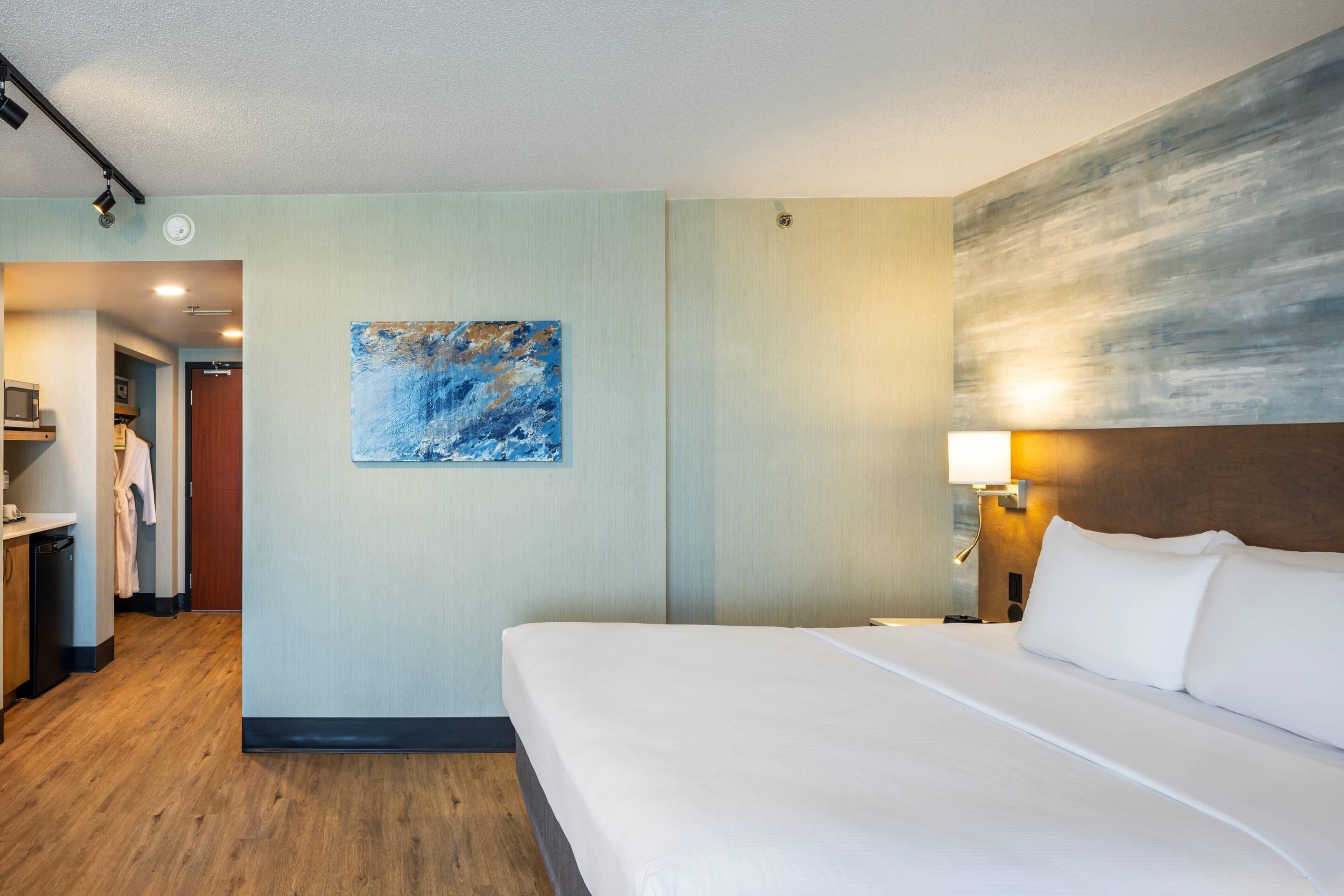 Una habitación de hotel con una cama grande, un cuadro en la pared y suelo de madera.
