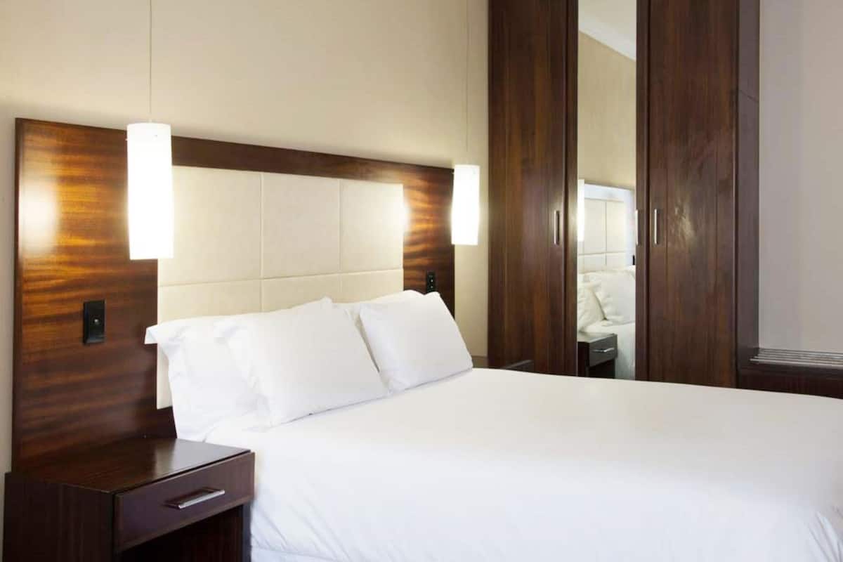 A hotel room with a large bed, wooden headboard, bedside tables, and a mirror.