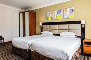 A hotel room with two beds, a wooden wardrobe, and abstract wall art.