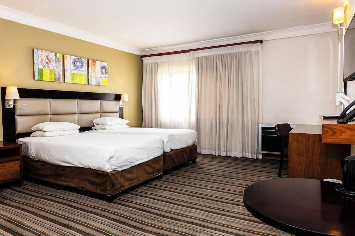 Une chambre d’hôtel avec un grand lit, un bureau, une chaise et une fenêtre avec des rideaux.