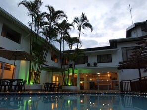 A poolside area with a pool, outdoor seating, and palm trees.