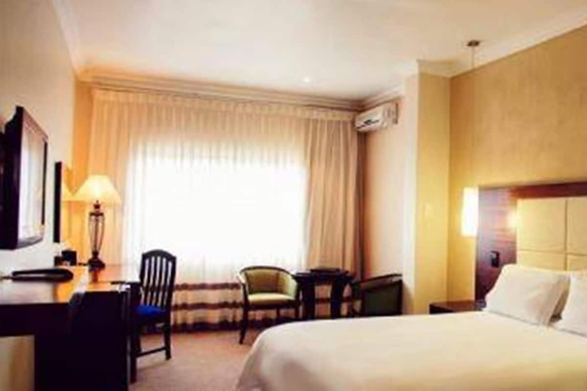 A hotel room with a large bed, a desk with a lamp, two chairs, and a window with curtains.