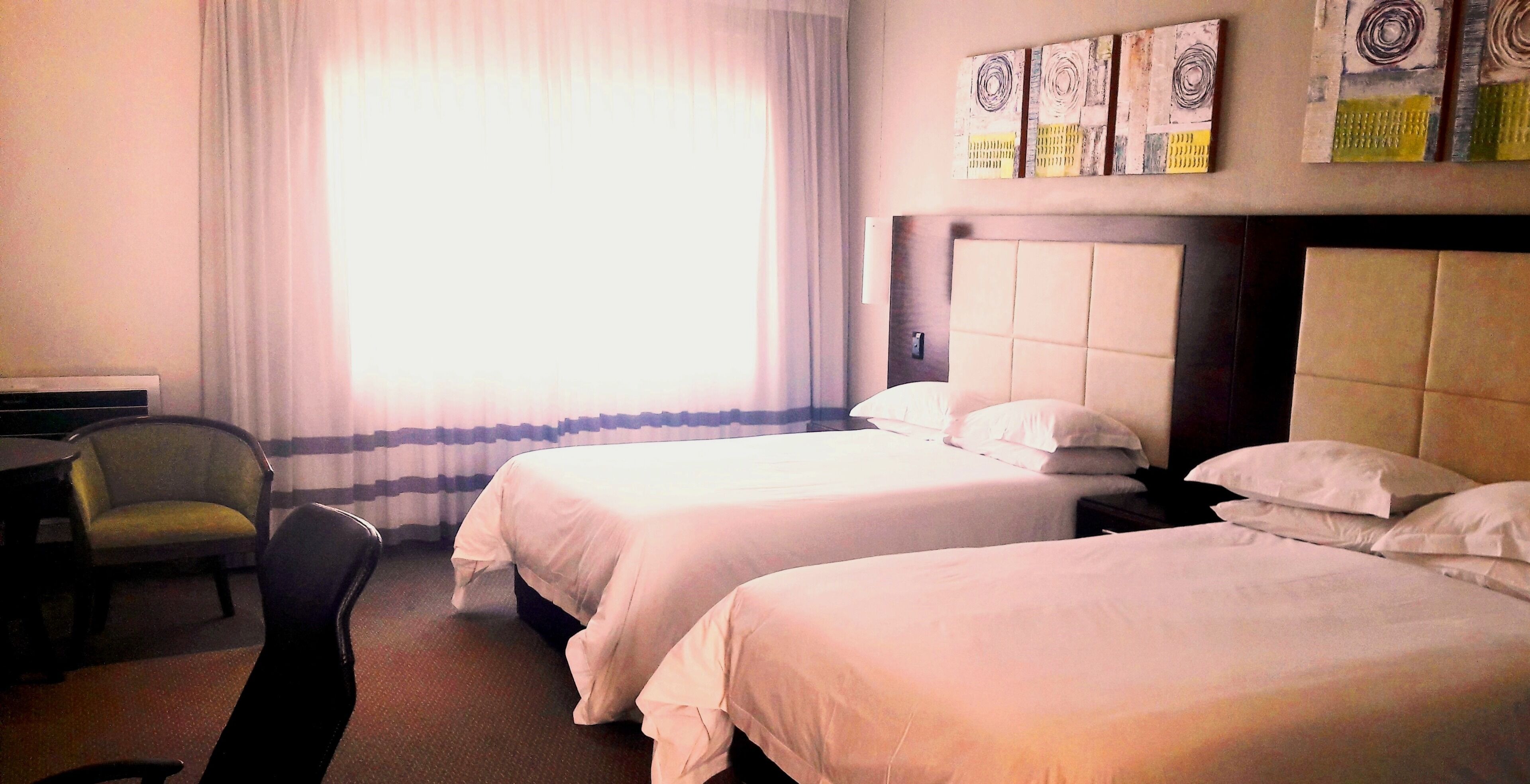 Habitación de hotel con dos camas, una silla, un escritorio y una ventana con cortinas.