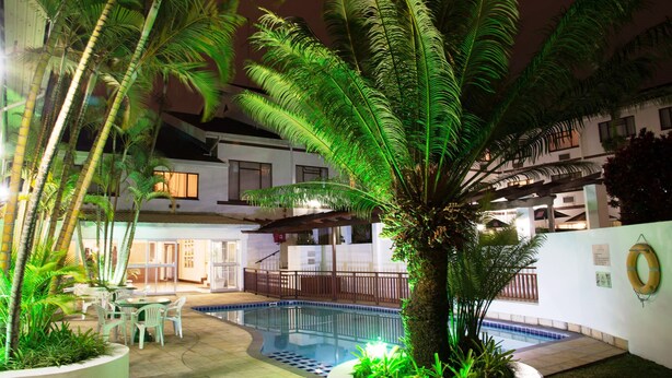 An outdoor swimming pool surrounded by palm trees and a covered seating area. - Premier Splendid Inn Pinetown (Pinetown)