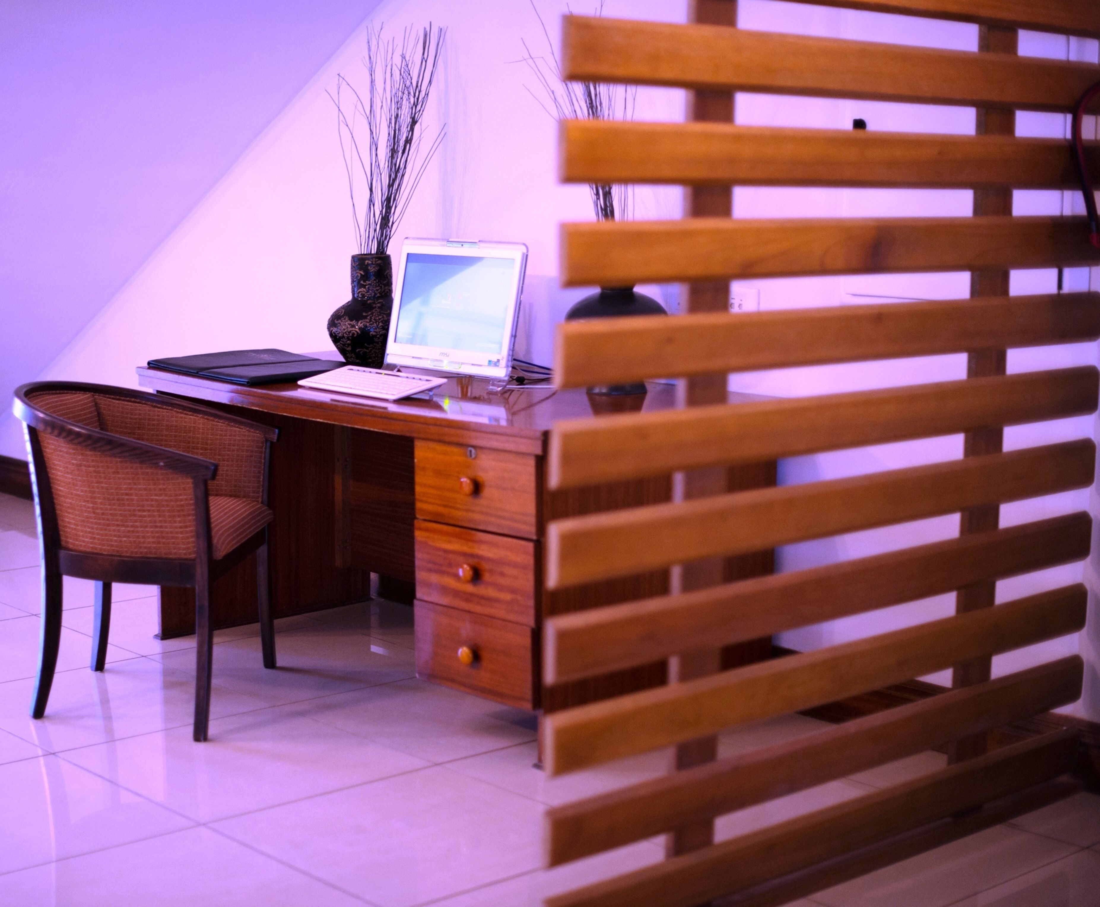 Un escritorio moderno con una laptop, un jarrón con ramas y una silla de madera.