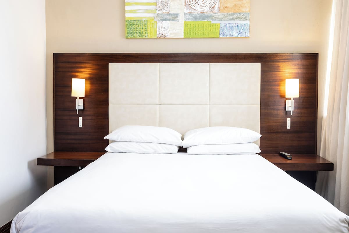A hotel room with a large bed, two bedside lamps, and a headboard with a textured panel.
