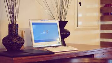A wooden desk with a laptop, two vases with branches, and a wicker chair.
