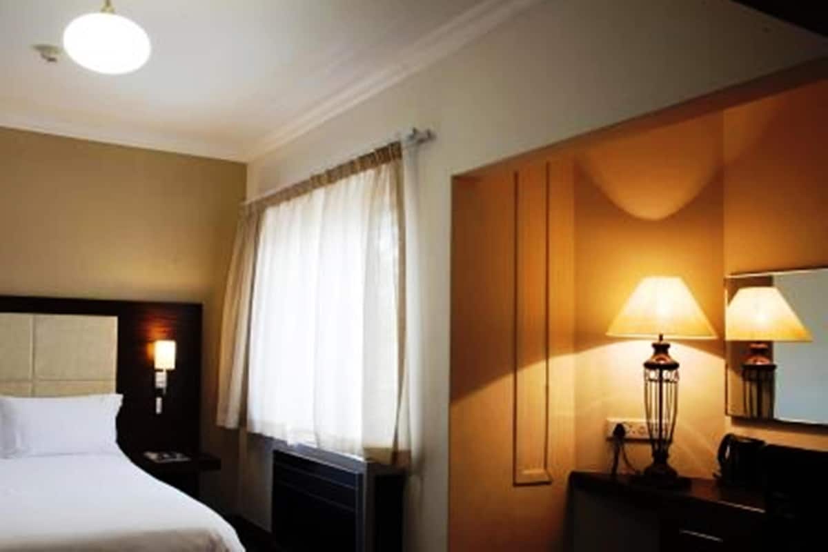 A hotel room with a bed, a nightstand, a lamp, and a wall-mounted mirror.