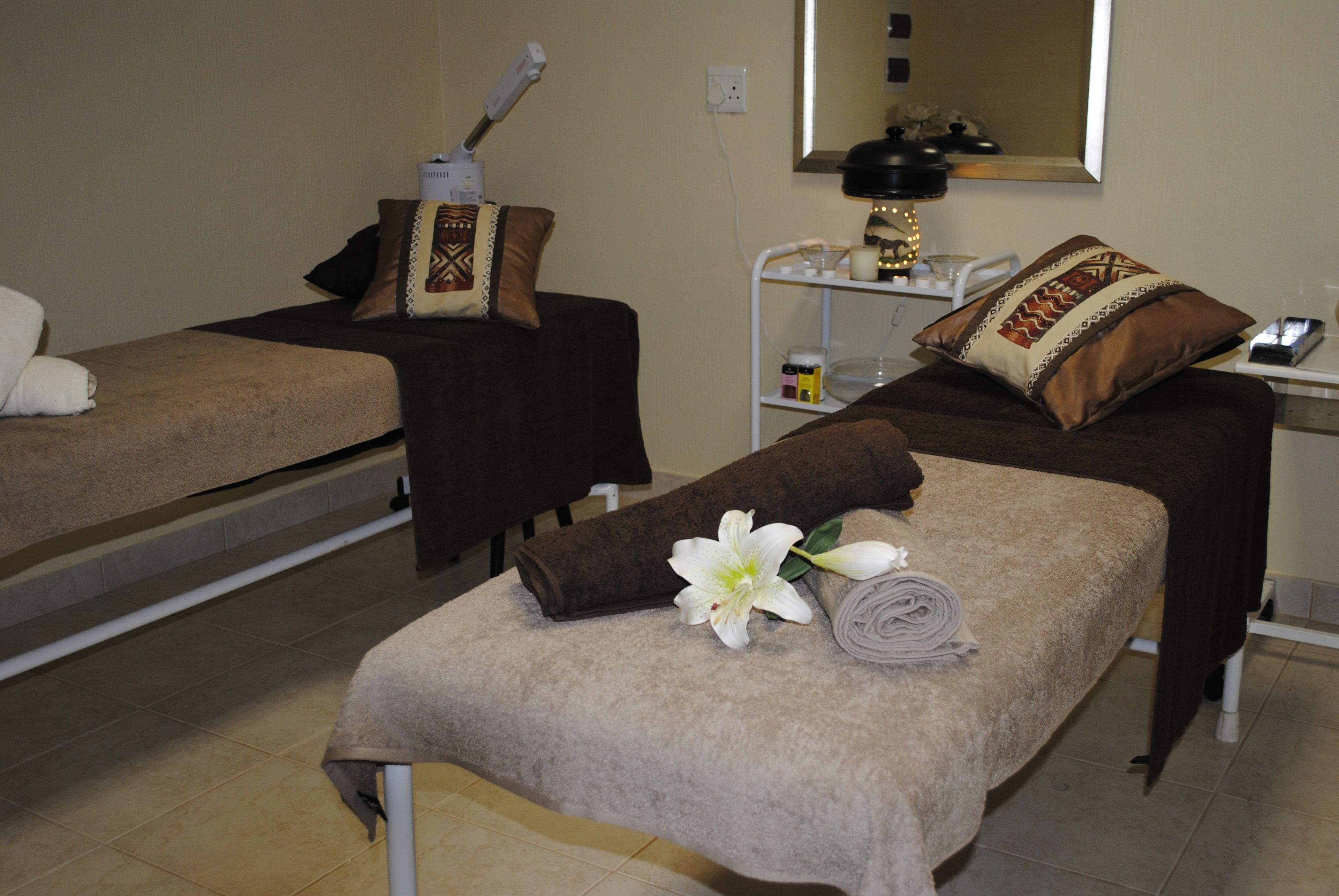 Una habitación con dos camas, cada una con toalla y almohada. Hay un espejo sobre las camas y una estantería con diversos objetos.