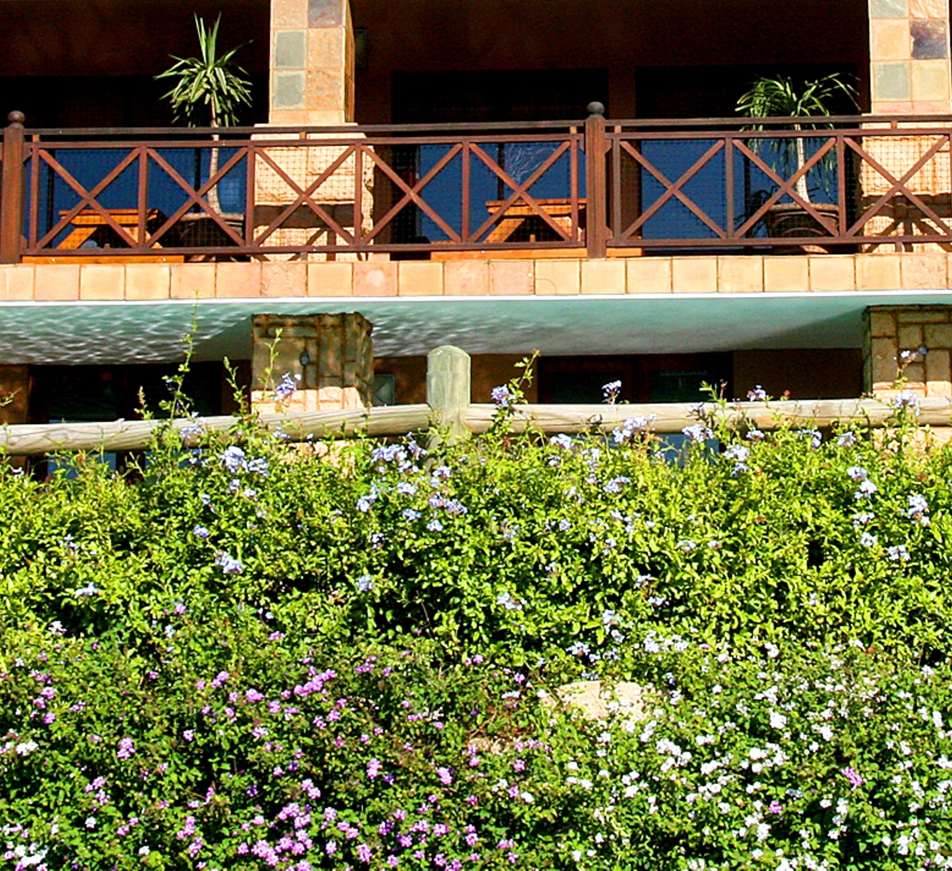 A hotel with a balcony, lush greenery, and a stone facade.
