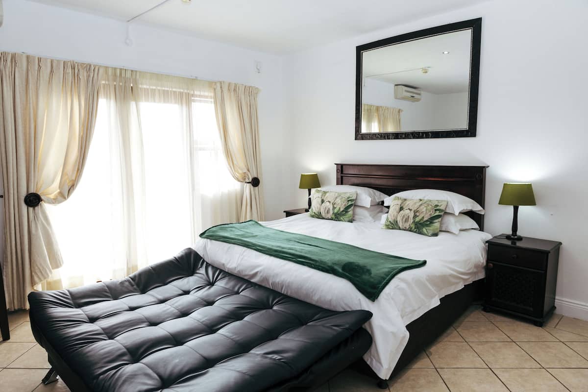 A bedroom with a bed, bedside lamps, a bench, a mirror, and curtains.