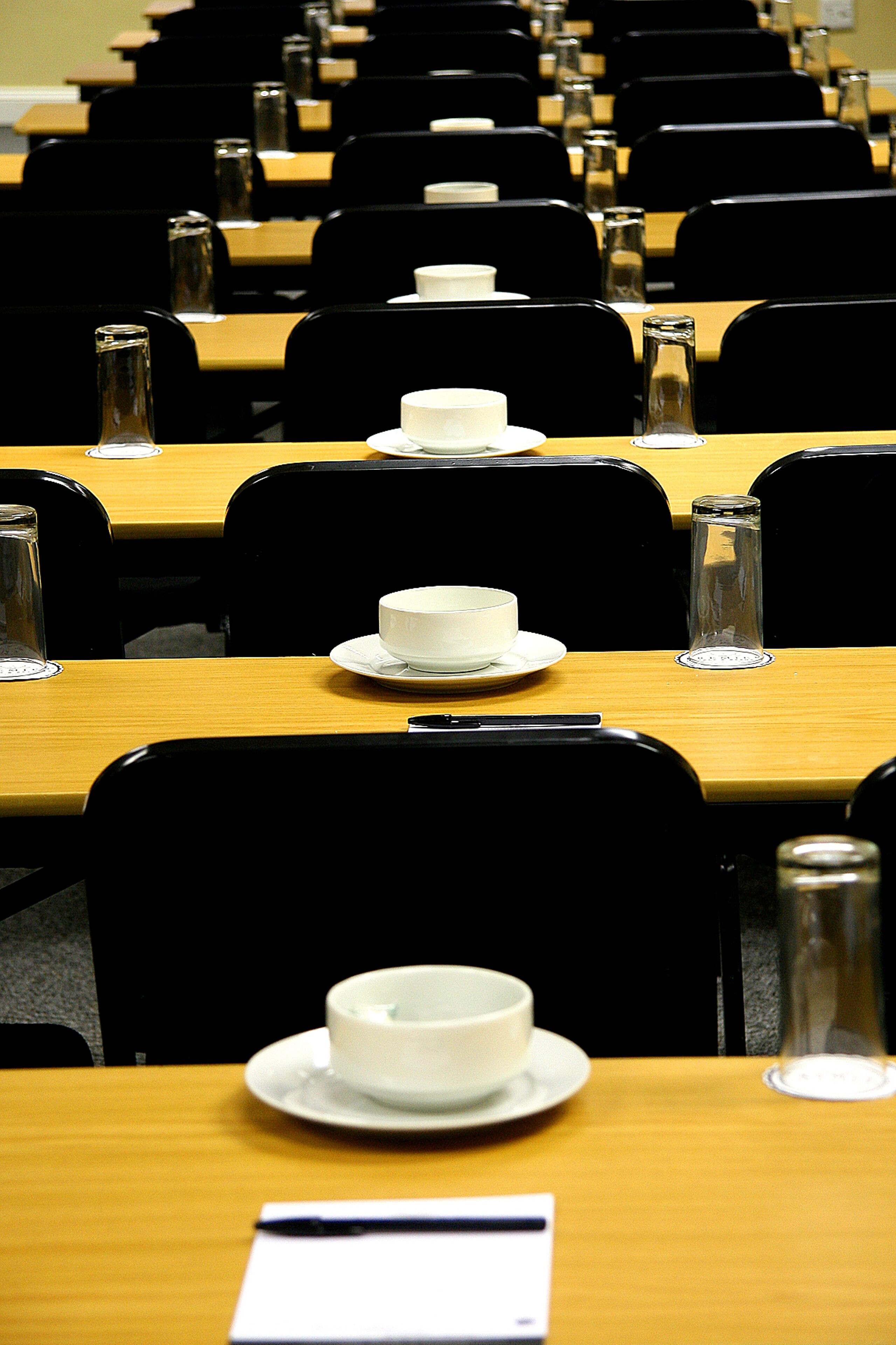 A conference room with rows of tables, each with a white cup and saucer, and a glass bottle.