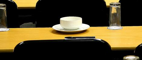 A conference room with rows of tables, each with a white cup and saucer, and a glass bottle.