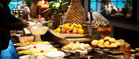 Buffet com diversos alimentos, incluindo frutas, doces e acompanhamentos.