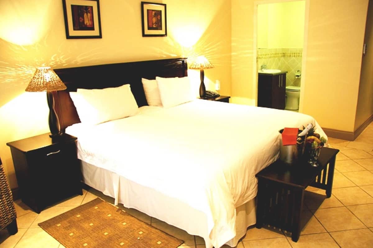 A hotel room with a large bed, two bedside tables, a nightstand, a small table with a lamp, and a mirror.