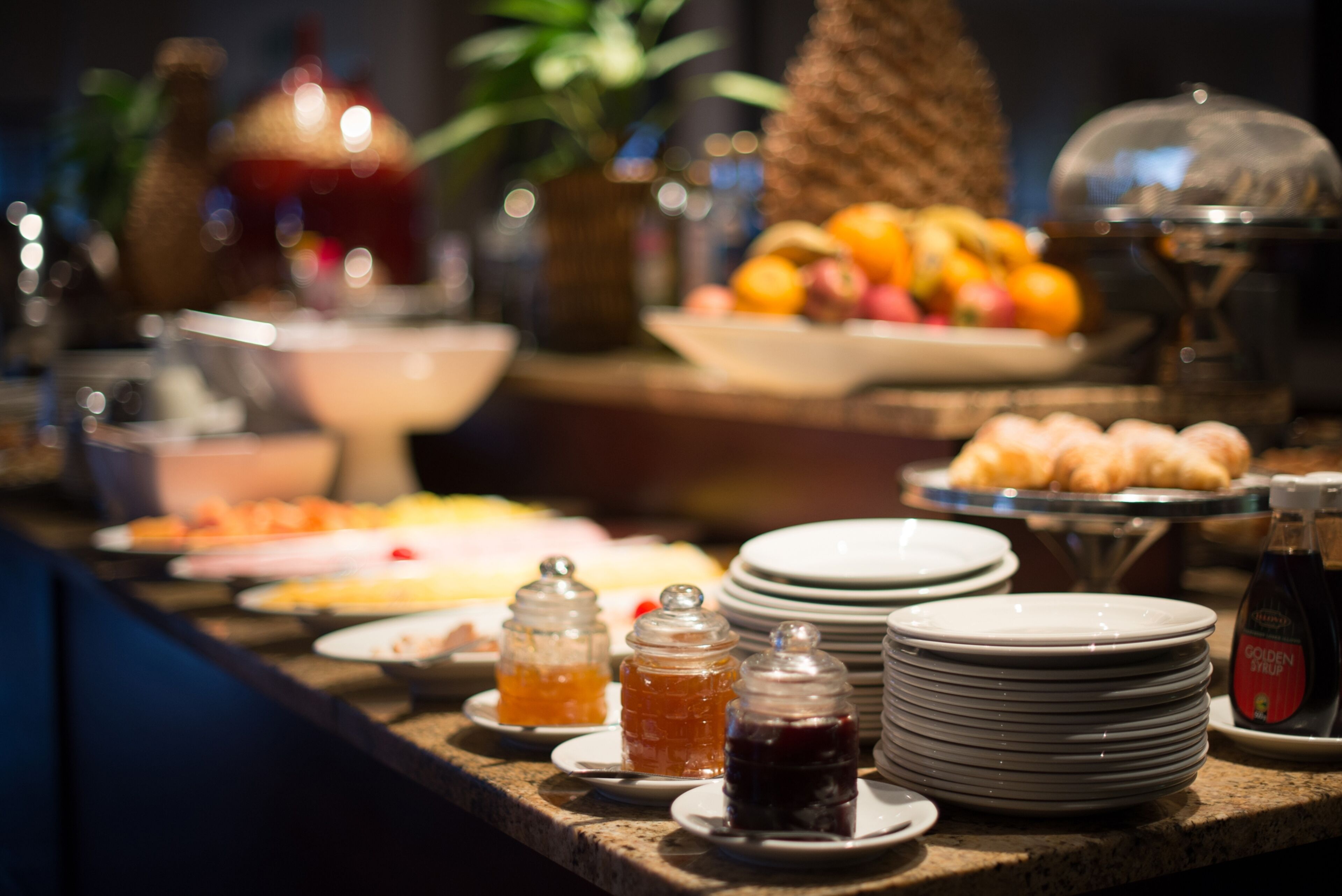 A buffet table with various food items, including fruits, pastries, and condiments.