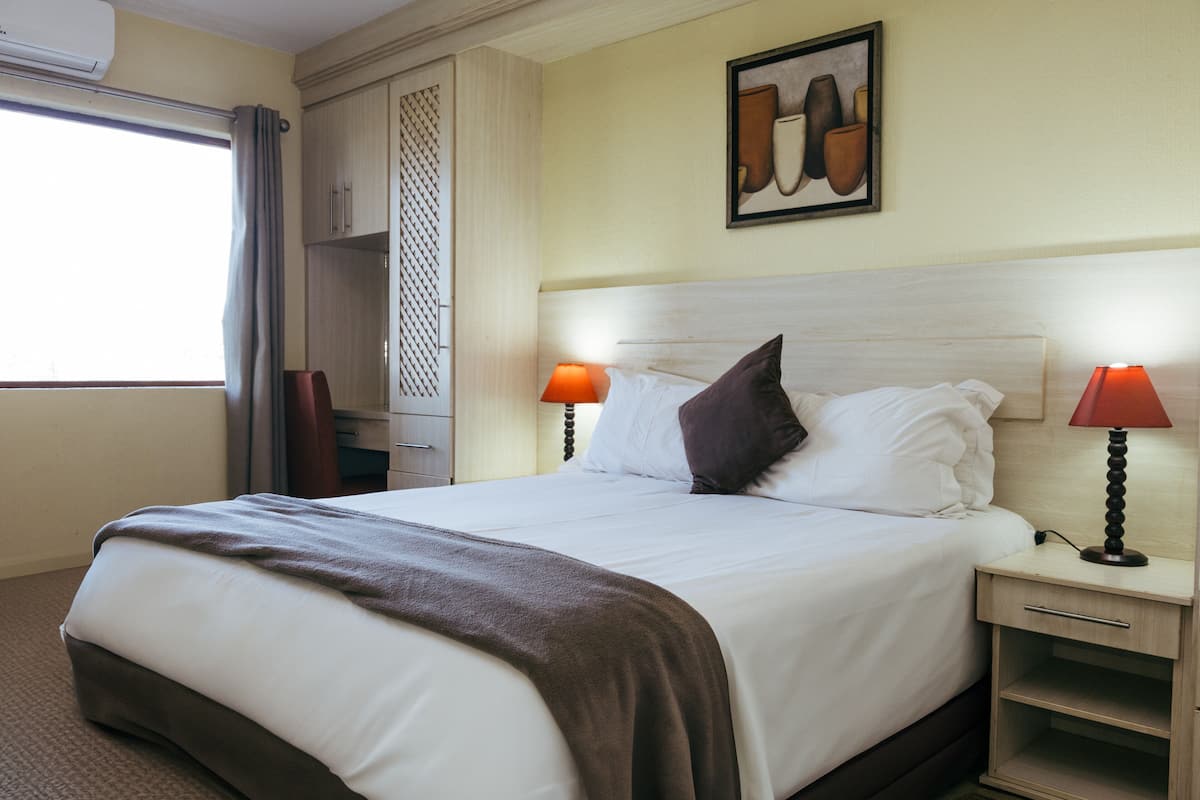 A neatly made bed with a brown throw blanket, two bedside lamps, and a wall-mounted artwork.