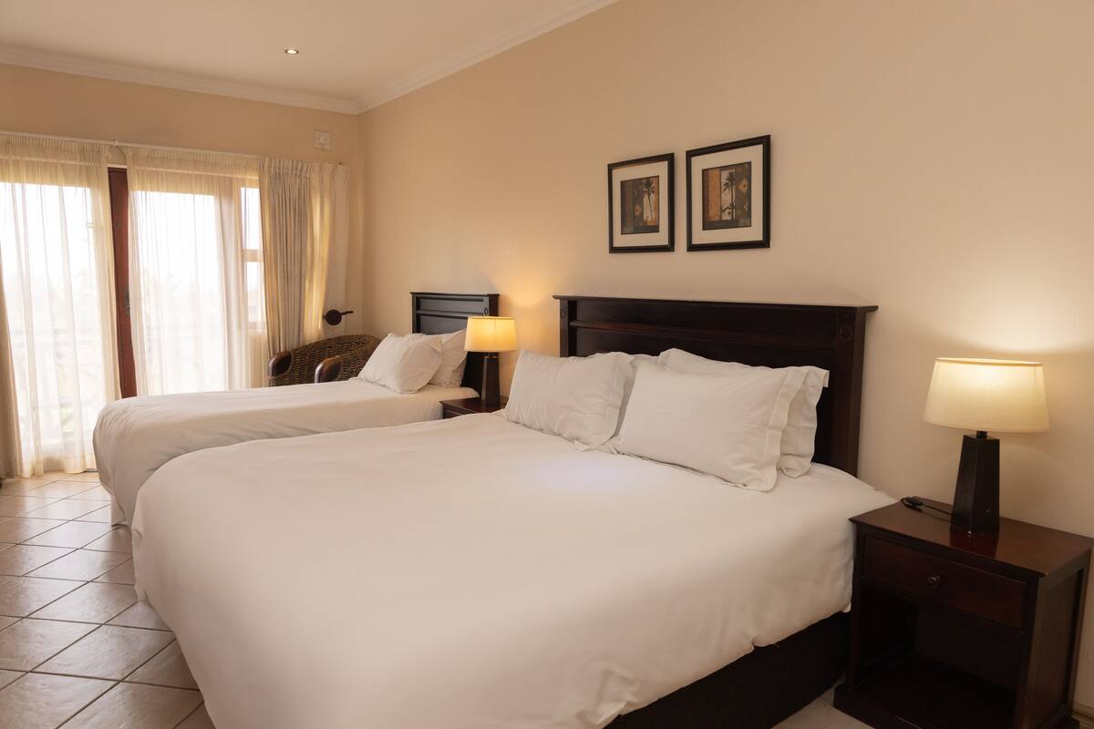 A hotel room with two beds, a nightstand with a lamp, and a wall-mounted picture.
