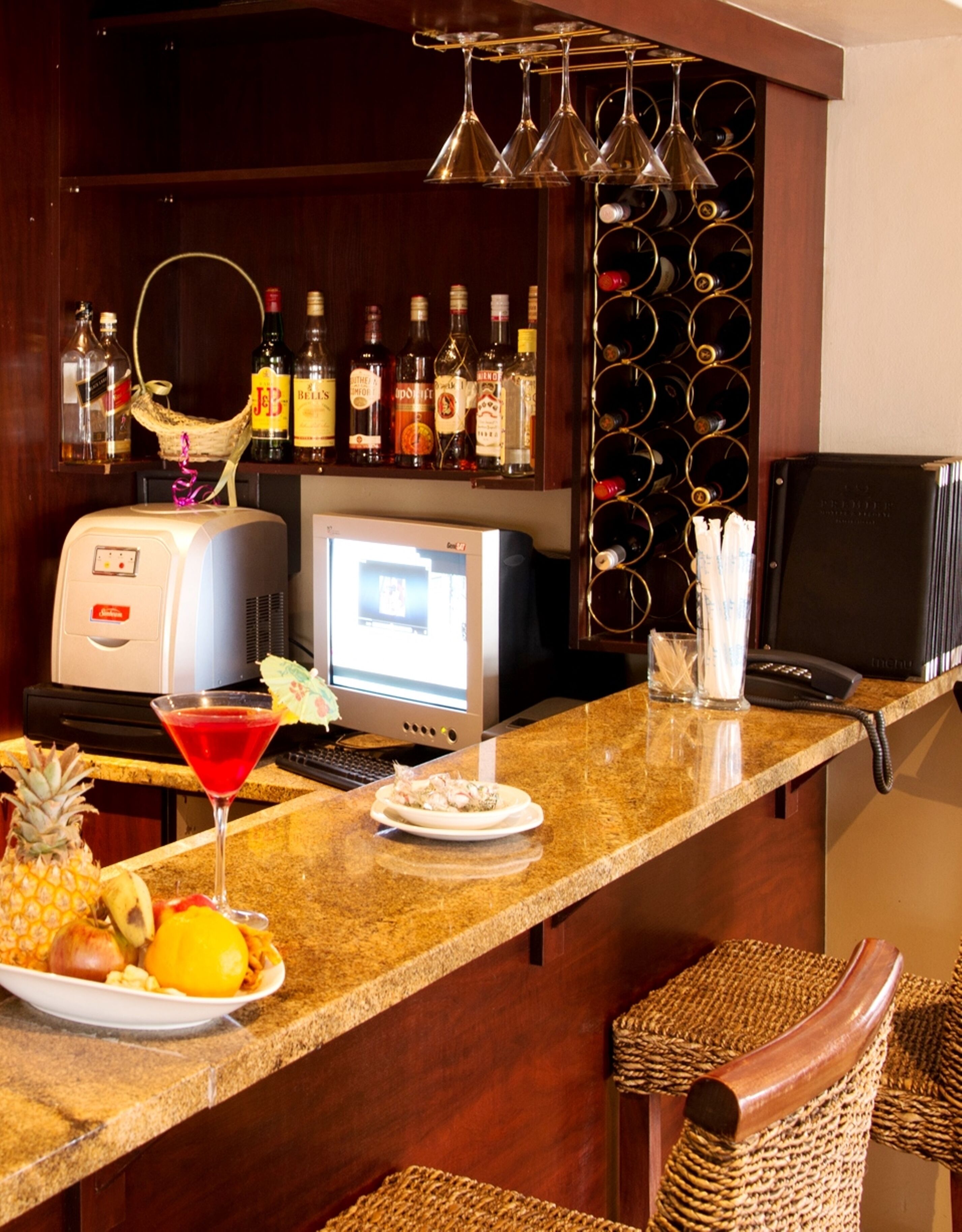A bar area with a computer, bottles, and a fruit platter.