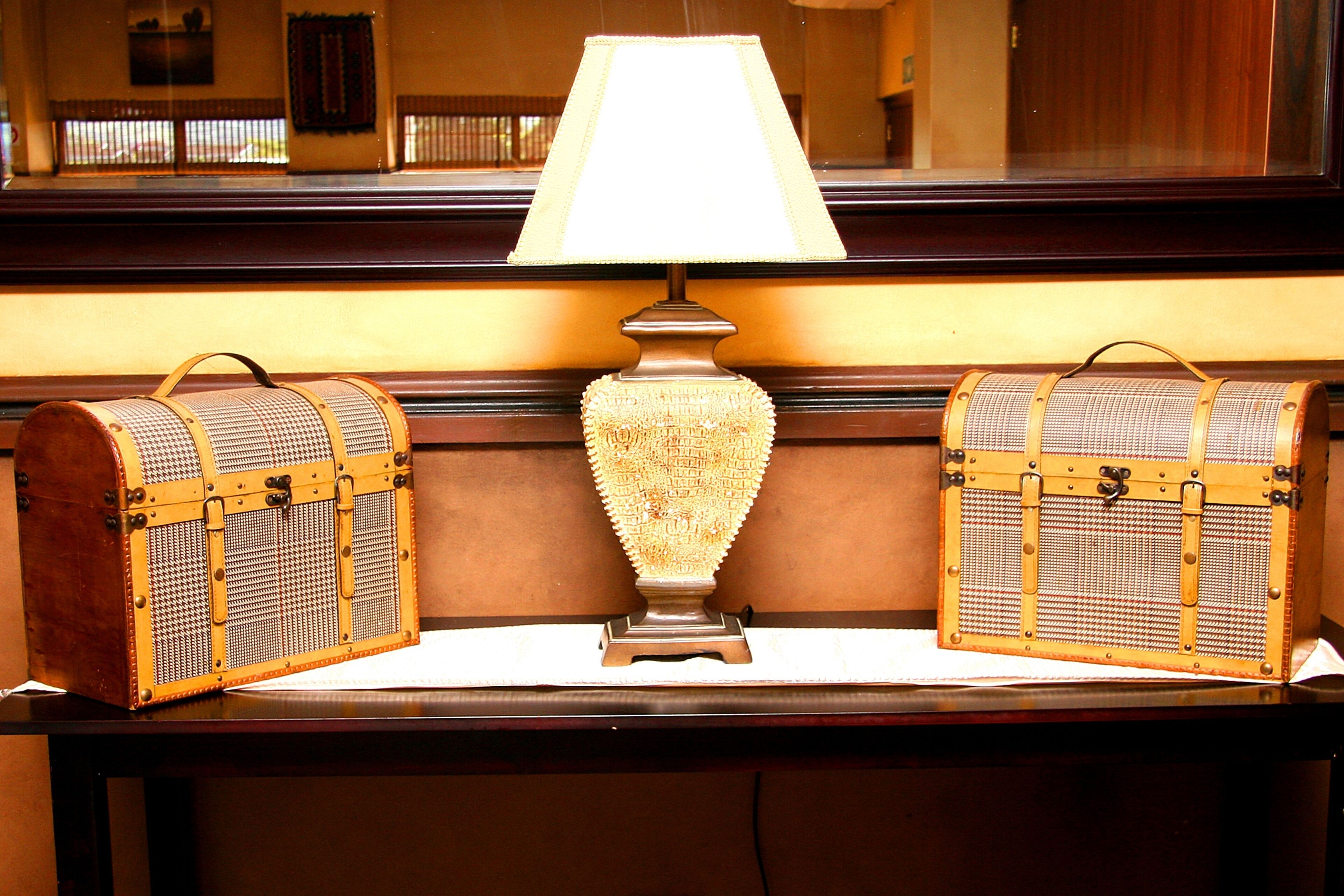A lamp with a white shade, two vintage-style trunks with handles, and a wooden bench.