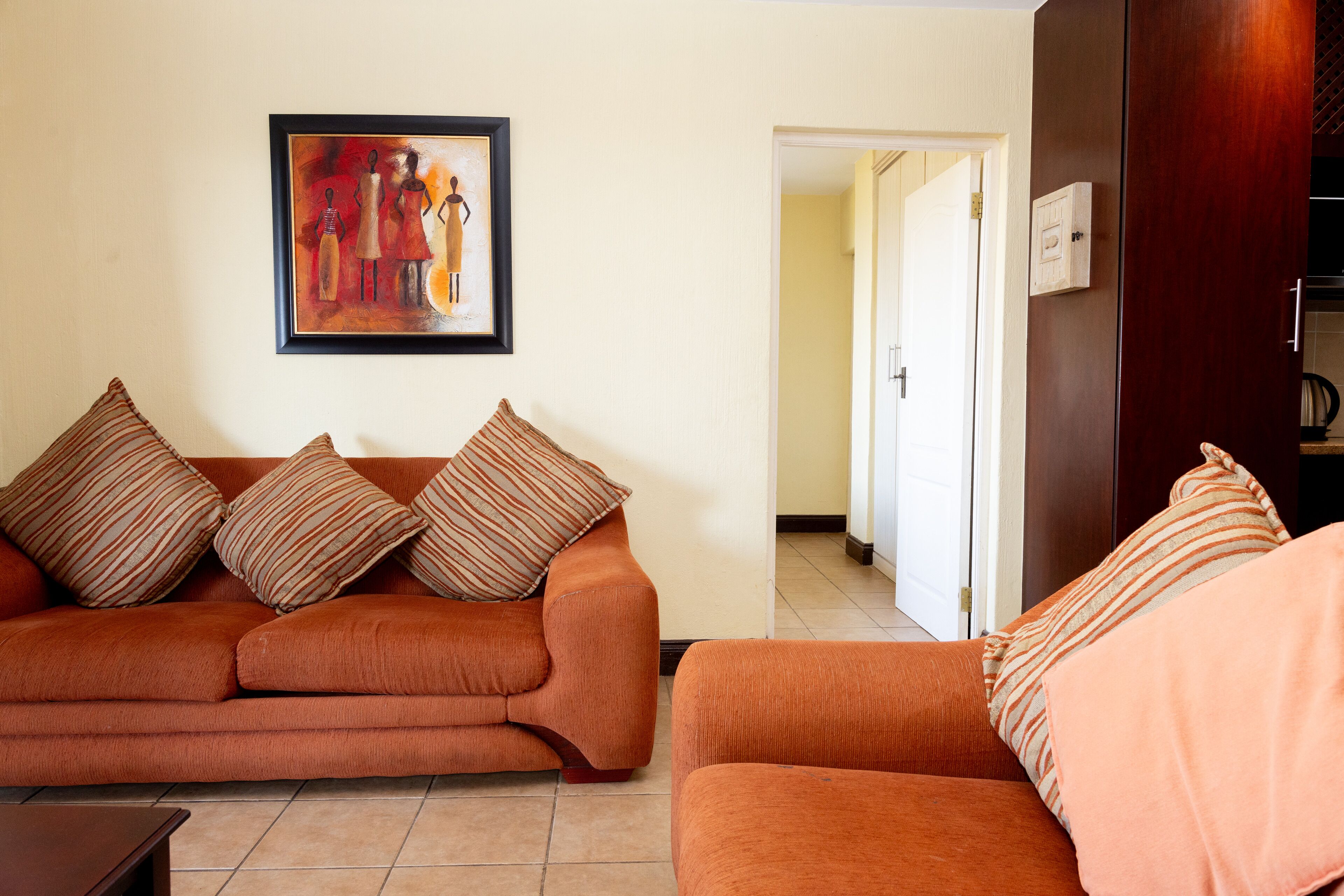A living room with a sofa and armchairs, a framed artwork on the wall, and a door leading to another room.