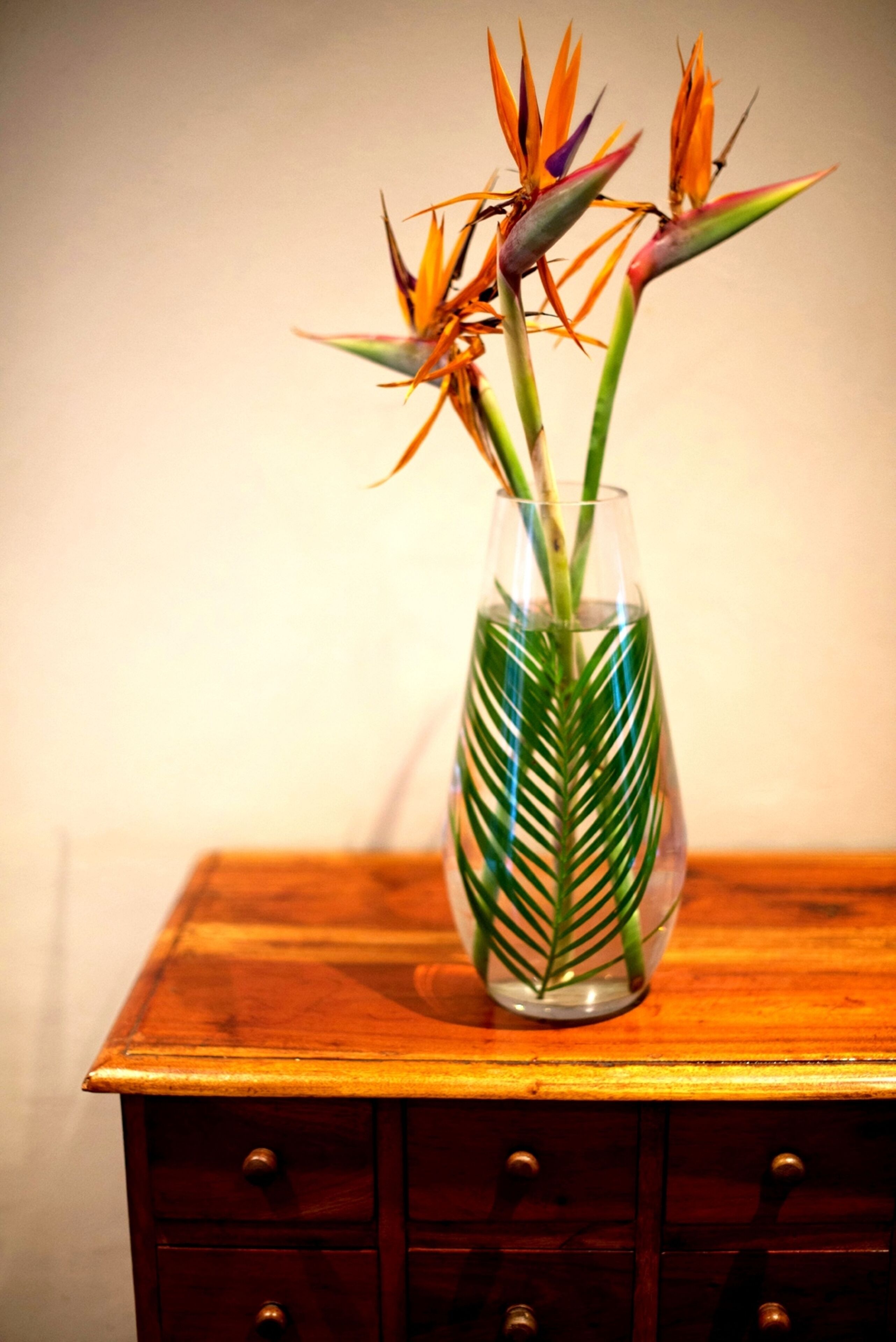 Un jarrón de vidrio transparente con diseño de hoja de palma sobre una mesa de madera.